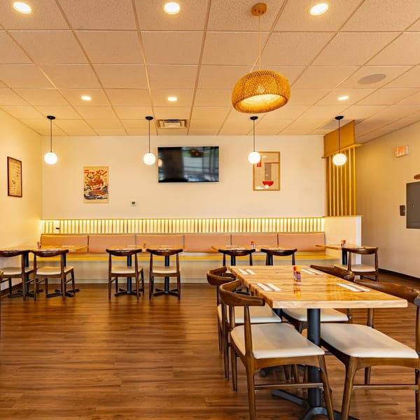 Interior of Shinjiru Ramen with wooden tables, chairs, and a long booth along the wall.