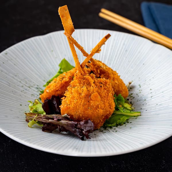 Three crispy fried shrimp skewers with green and red lettuce on a white plate with chopsticks.