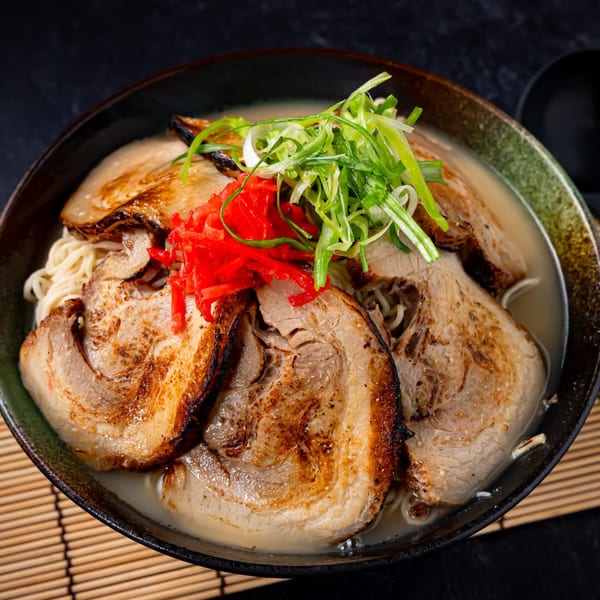 Shinjiru Ramen bowl with chashu pork, green onions, and red pickled ginger on a bamboo mat.