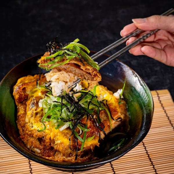 Chopsticks lifting a piece of crispy fried pork and rice from a bowl of Katsudon.