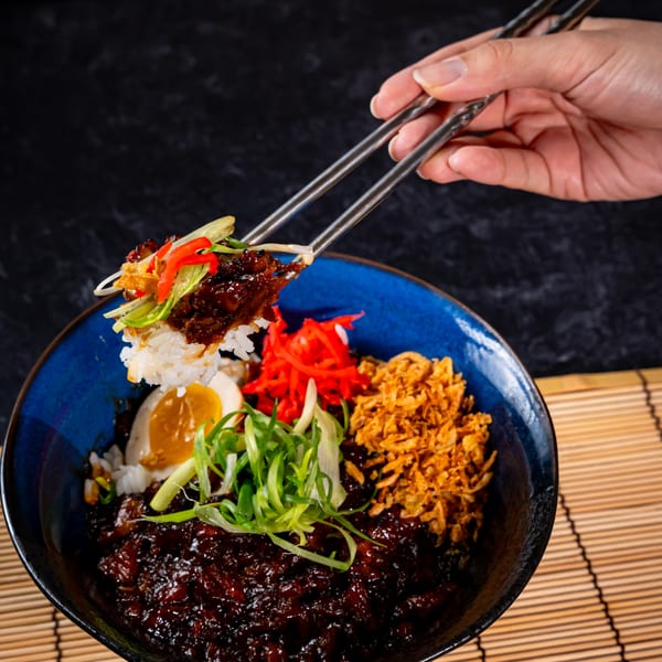 Chopsticks lifting rice and dark meat from a bowl with egg, red ginger, and fried onions.