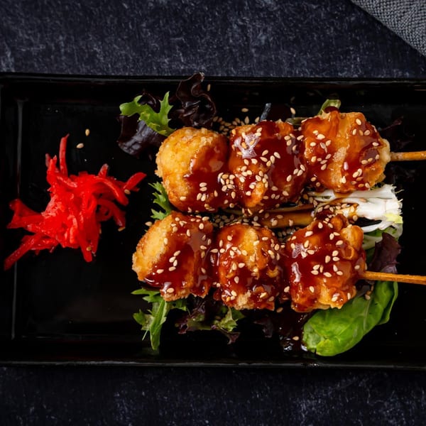 Two skewers of crispy fried chicken with teriyaki glaze and sesame seeds, served with pickled ginger.
