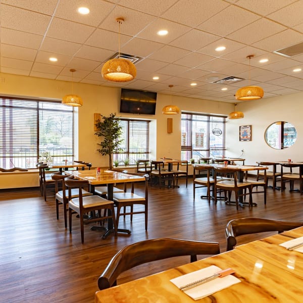 Interior of Shinjiru Ramen restaurant with wooden tables and chairs, large windows, and woven pendant lights.