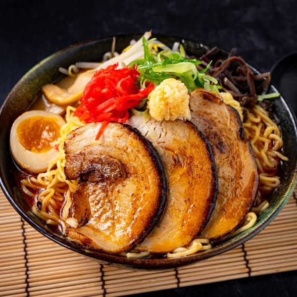 Shinjiru Ramen bowl with pork slices, egg, noodles, and various toppings on a bamboo mat.