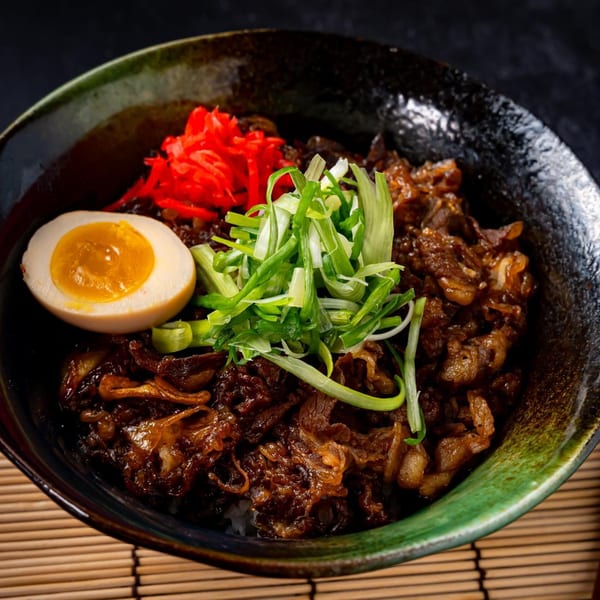 A bowl of Shinjiru Ramen's gyudon, topped with sliced beef, green onions, pickled ginger, and a soft-boiled egg.