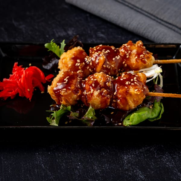 Two skewers of fried chicken with teriyaki sauce and sesame seeds, served with red pickled ginger.