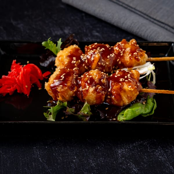 Two skewers of fried chicken with teriyaki sauce and sesame seeds, served with pickled ginger.