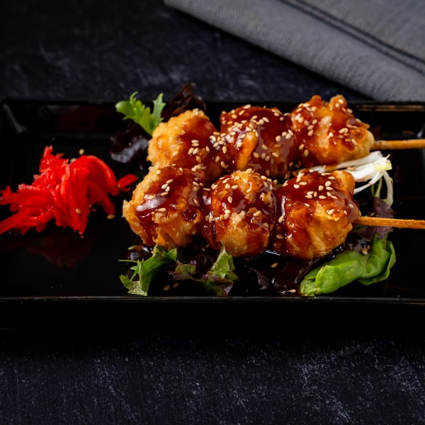 Shinjiru Ramen's fried chicken skewers with teriyaki sauce, sesame seeds, and pickled ginger on a black plate.