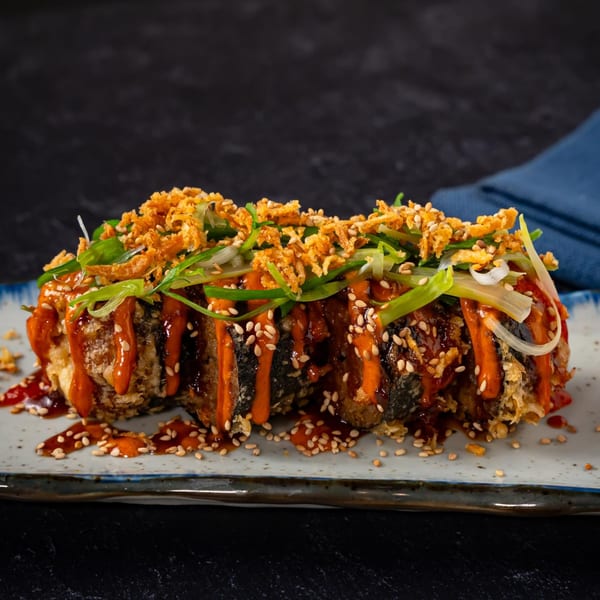 Crispy Shinjiru Ramen sushi roll drizzled with sauce, sesame seeds, fried onions, and scallions.