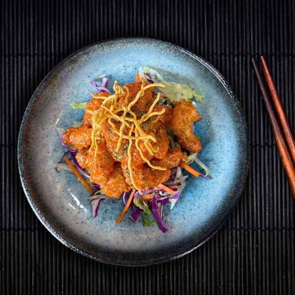 Shinjiru Ramen's crispy shrimp appetizer with orange sauce, fried noodles, and colorful salad on a blue plate.