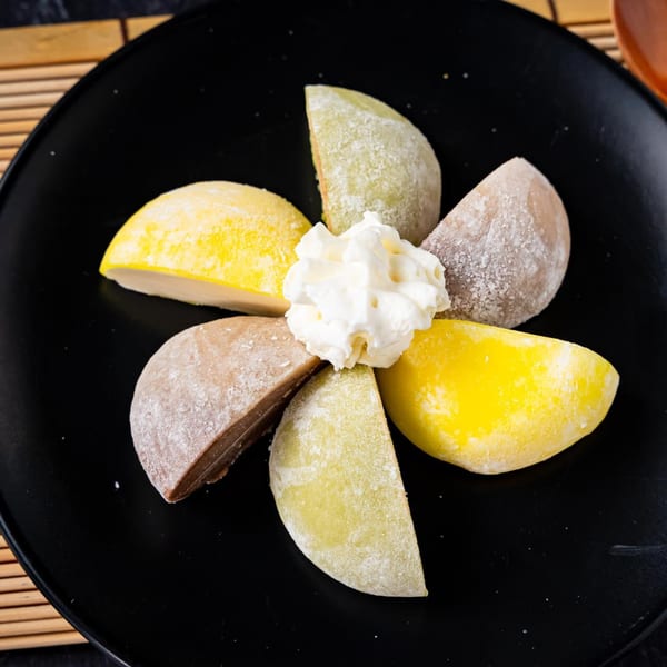 Assorted mochi ice cream, including yellow, green, and brown flavors, arranged with whipped cream.