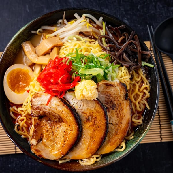 A bowl of Shinjiru Ramen with pork, egg, noodles, and various toppings on a bamboo mat.