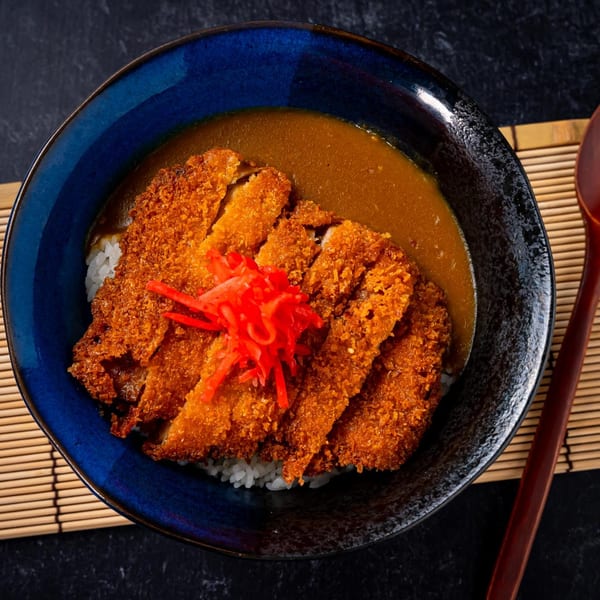 Shinjiru Ramen's katsu curry with crispy fried chicken, rice, and red pickled ginger in a blue bowl.