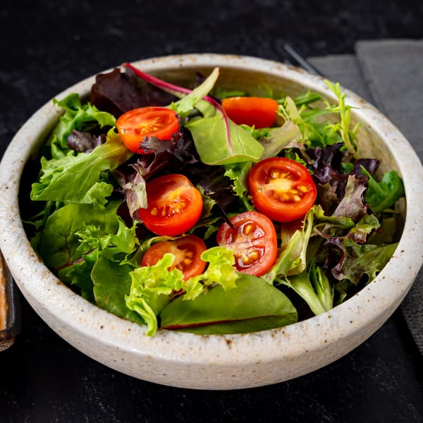 Fresh green and red lettuce salad with halved cherry tomatoes in a rustic bowl.