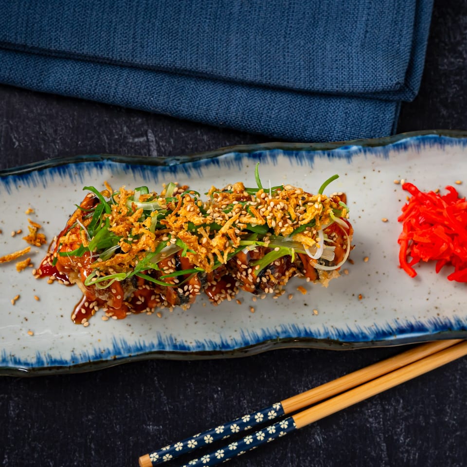 Shinjiru Ramen's crispy eel sushi roll with sauce, sesame seeds, scallions, and red ginger.