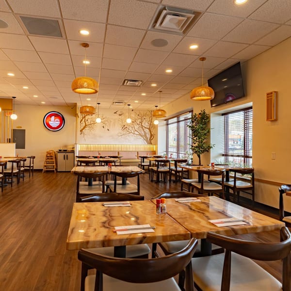 Shinjiru Ramen dining room with wooden tables, chairs, and a wall mural of a tree.