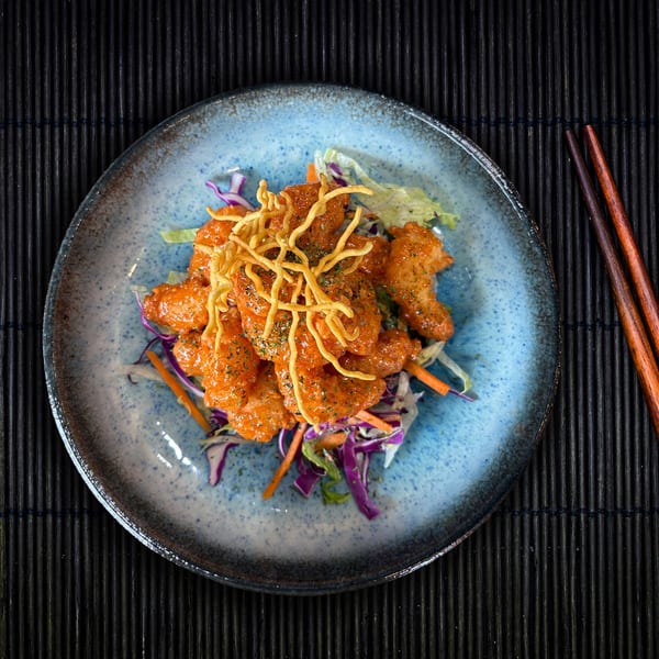 Shinjiru Ramen's spicy shrimp tempura with crispy noodles and fresh cabbage on a blue plate.