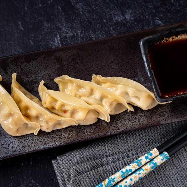 Shinjiru Ramen's gyoza dumplings with dipping sauce and chopsticks on a dark textured plate.