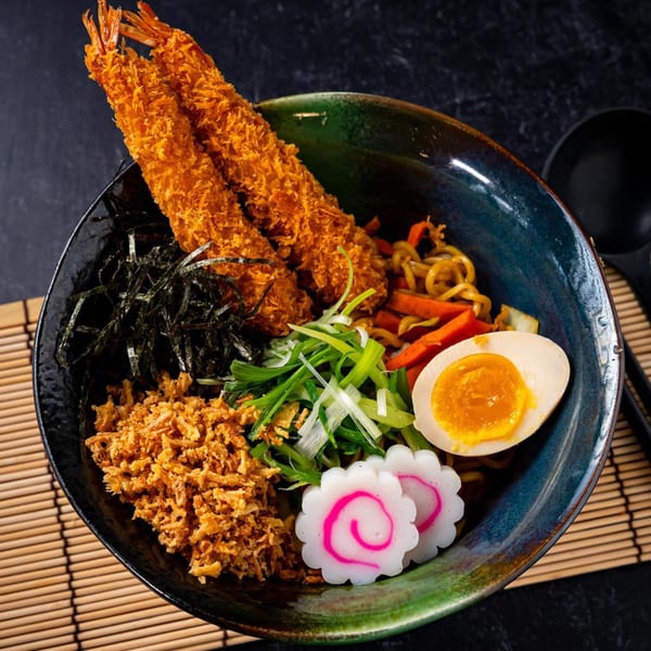 Shinjiru Ramen bowl with crispy shrimp, noodles, egg, scallions, fish cake, and seaweed on a bamboo mat.