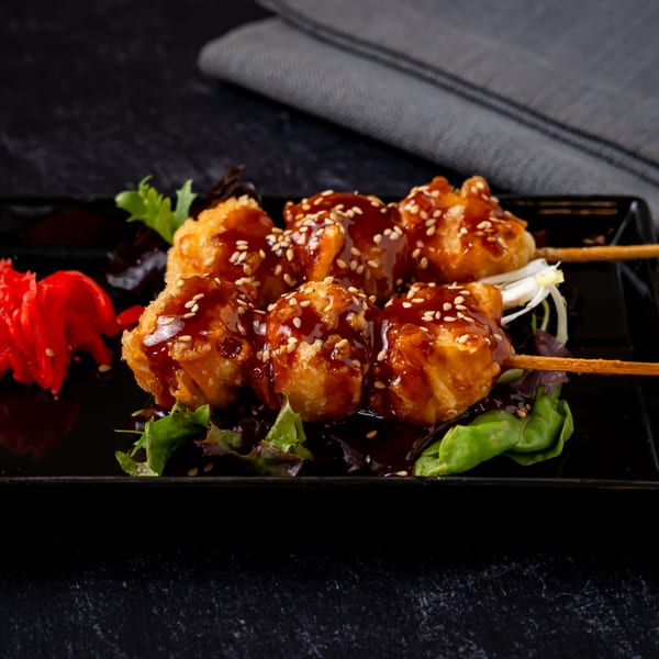 Shinjiru Ramen's fried dumplings on skewers, drizzled with sauce and sesame seeds, served with pickled ginger.