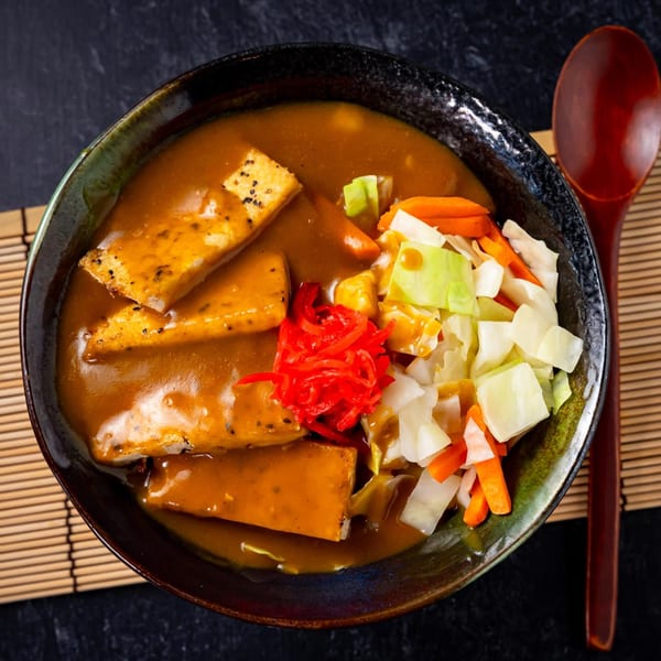 Shinjiru Ramen's curry ramen with tofu, red ginger, cabbage, and carrots in a dark bowl.