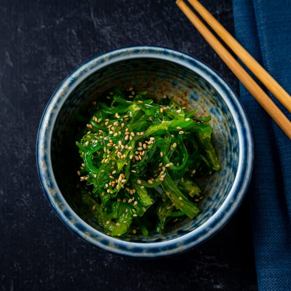 Shinjiru Ramen's wakame seaweed salad with sesame seeds in a blue bowl, with chopsticks.