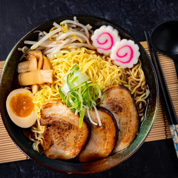 A bowl of Shinjiru Ramen with noodles, pork, egg, bamboo shoots, bean sprouts, and narutomaki.