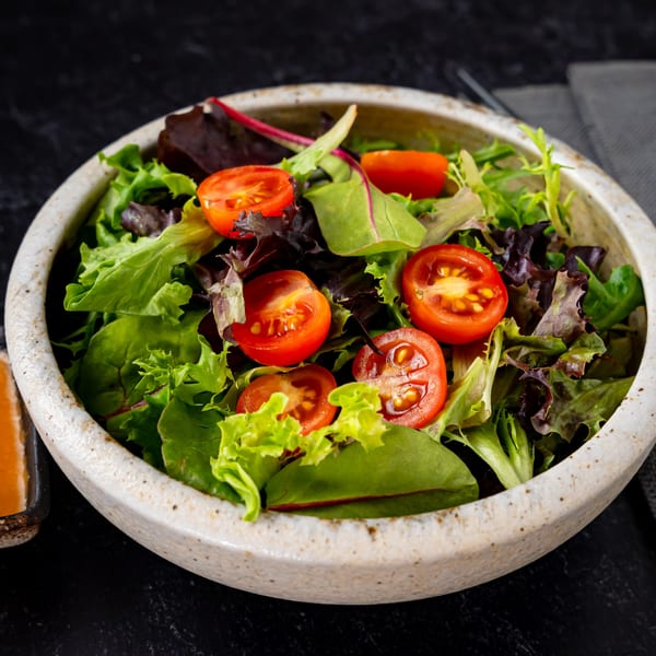 A fresh side salad with mixed greens and halved cherry tomatoes in a ceramic bowl.