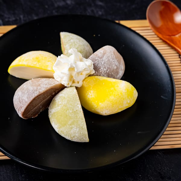 Assorted mochi, some cut in half, with whipped cream on a black plate.