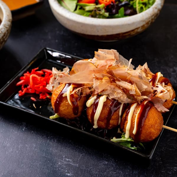 Shinjiru Ramen's takoyaki, drizzled with sauce and mayonnaise, topped with bonito flakes and red ginger.