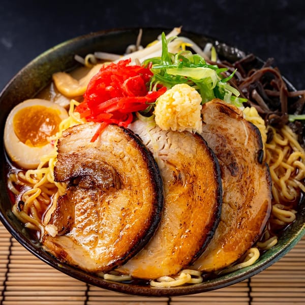 Shinjiru Ramen bowl with noodles, sliced pork, egg, red ginger, and green onions on a bamboo mat.