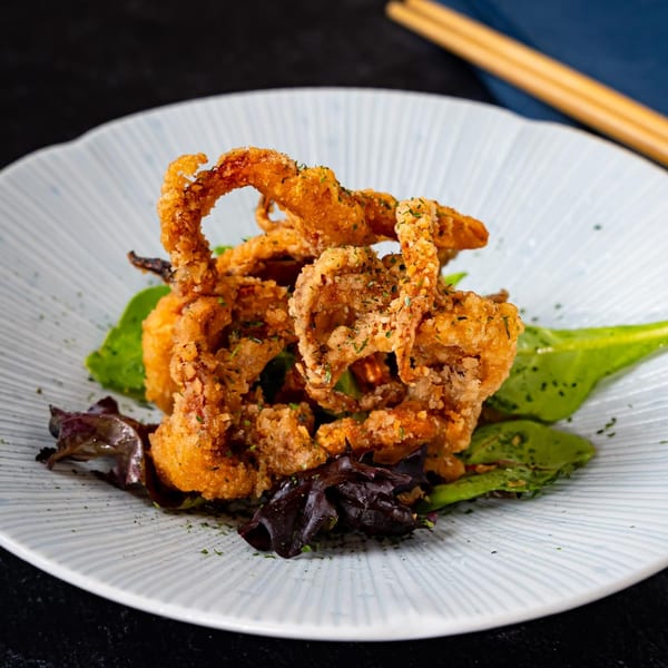 Crispy fried calamari, garnished with herbs, served on a bed of fresh green and red lettuce.