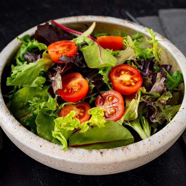 Fresh green and red leaf lettuce salad with halved cherry tomatoes in a rustic bowl.
